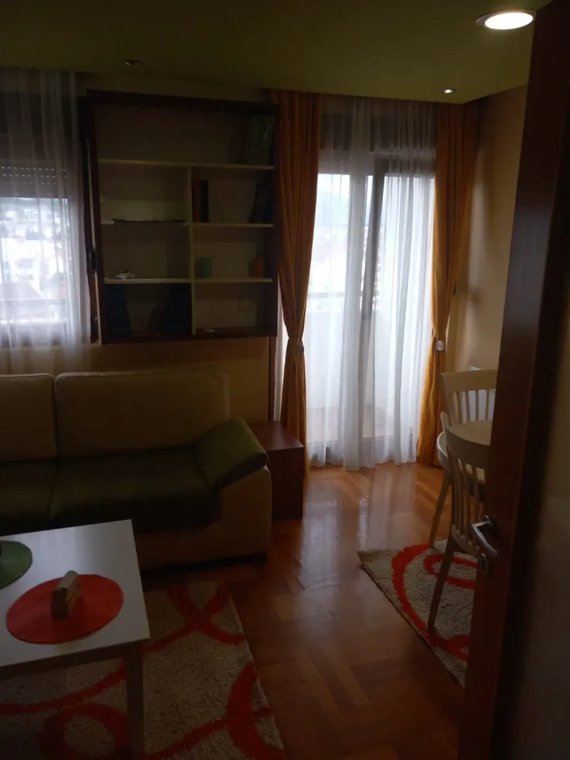 Dnevna soba sa garniturom za sjedenje, policom za knjige i trpezarijskim stolom pored prozora.