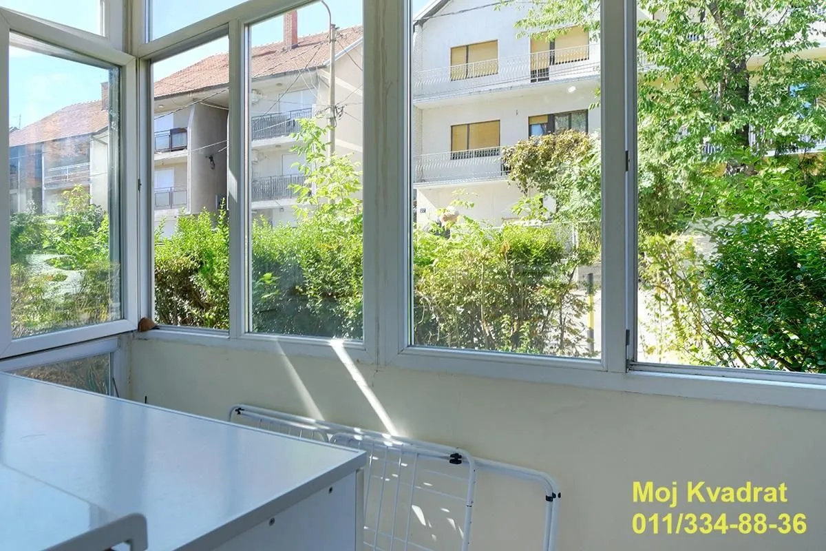 Zastakljeni balkon sa pogledom na okolne zgrade i zelenilo.