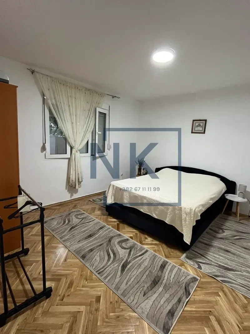 Bedroom with a double bed, parquet flooring, and a window with curtains.