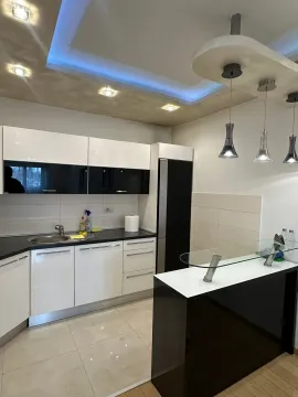 Moderna kuhinja sa bijelim elementima, crnim radnim površinama i šankom. - image 3