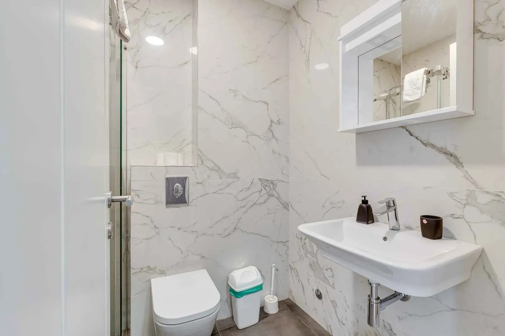 Modernly equipped bathroom with white marble tiles, washbasin and toilet.