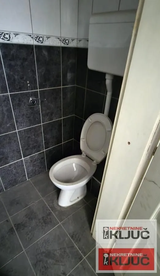 View of the bathroom with a toilet and dark tiles.