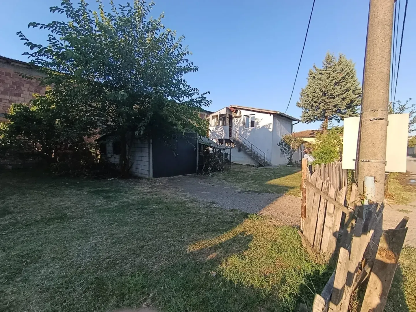 Pogled na dvorište porodične kuće sa pomoćnim objektom i zelenilom.