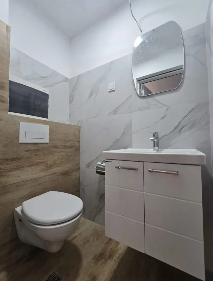 Moderne kupatilo sa ugradnom šoljom, umivaonikom i ogledalom.