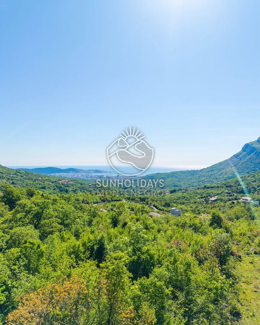 Pogled na zelenilo, brda i more u daljini.
