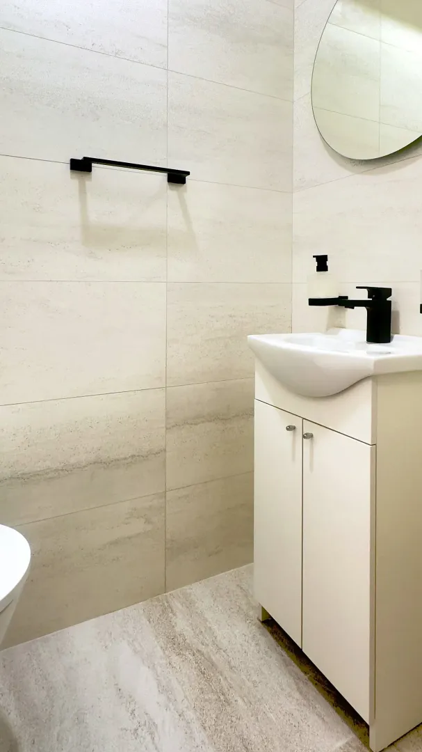 Modern bathroom with a white sink, black fixtures, and a round mirror.