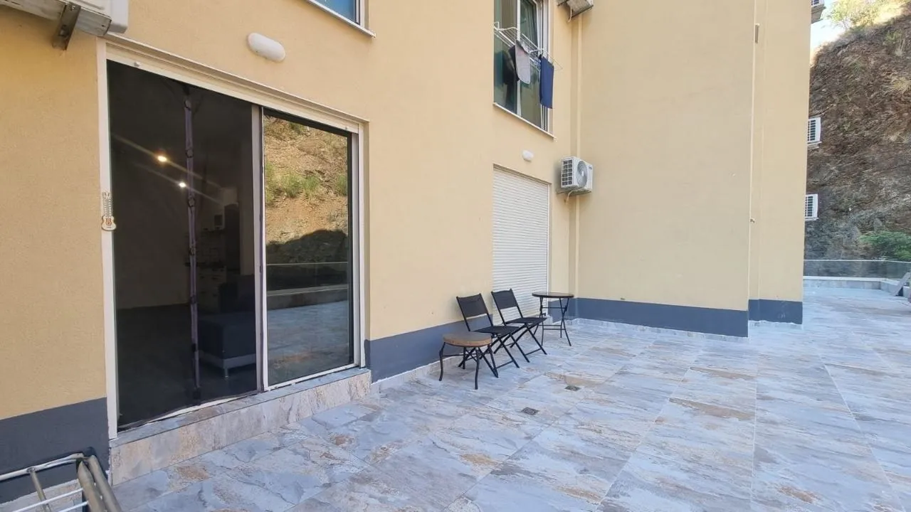 Terasa sa popločanim podom i garniturom za sedenje ispred ulaza u stan.
