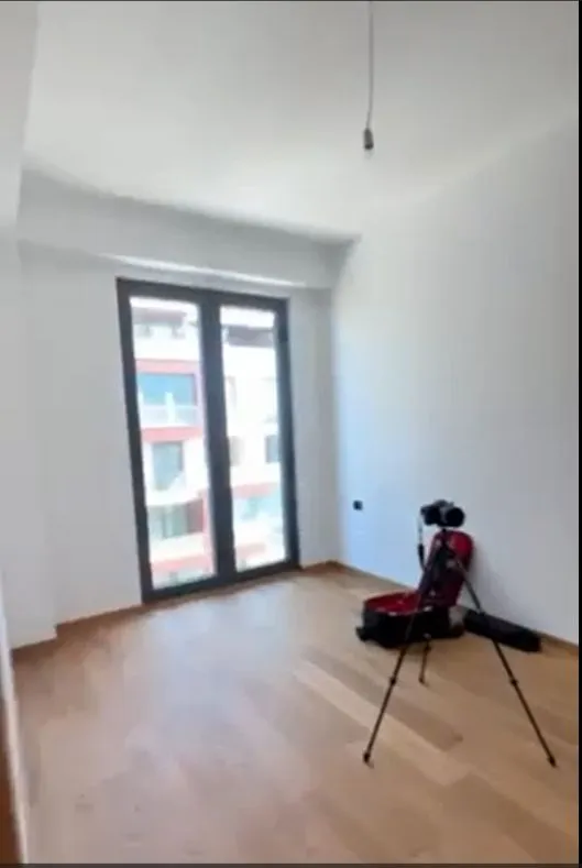 Prazna, svijetla soba sa drvenim podom i velikim balkonskim prozorom.