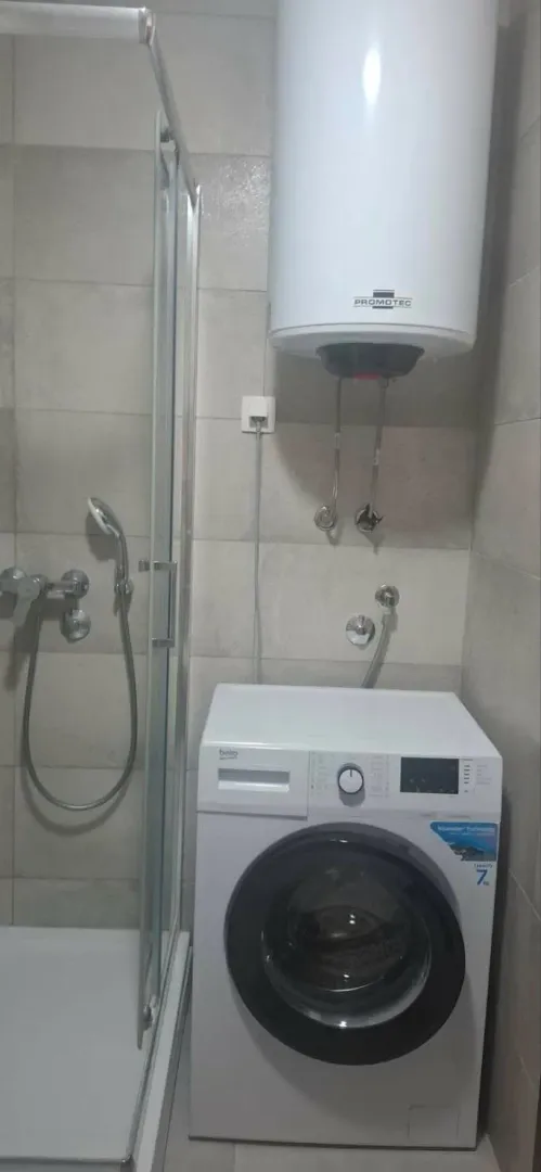 Pogled na kupatilo sa tuš kabinom, mašinom za veš i bojlerom.