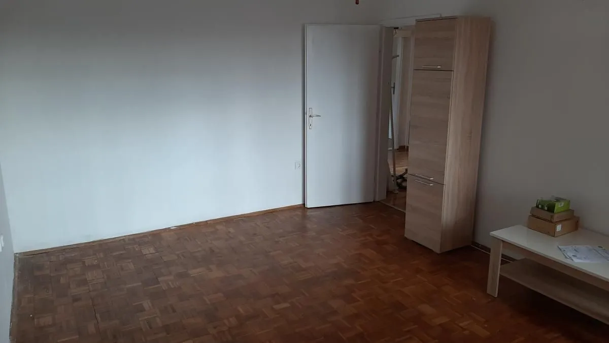 Prazna soba sa parketom na podu i belim zidovima.