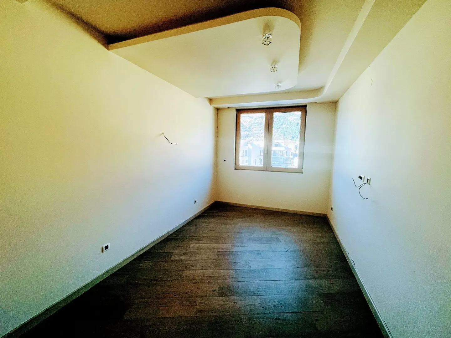 An empty room with a suspended ceiling and dark floors.