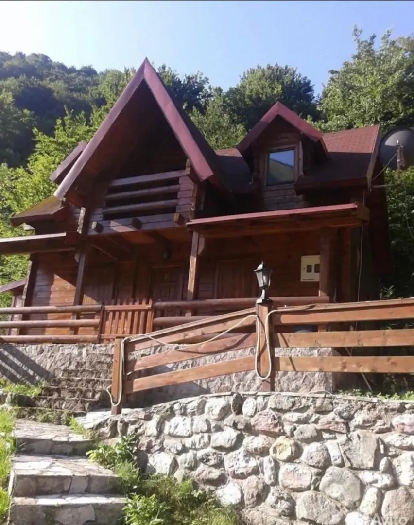 Eksterijer drvene vikendice sa kamenim temeljom i stepeništem.