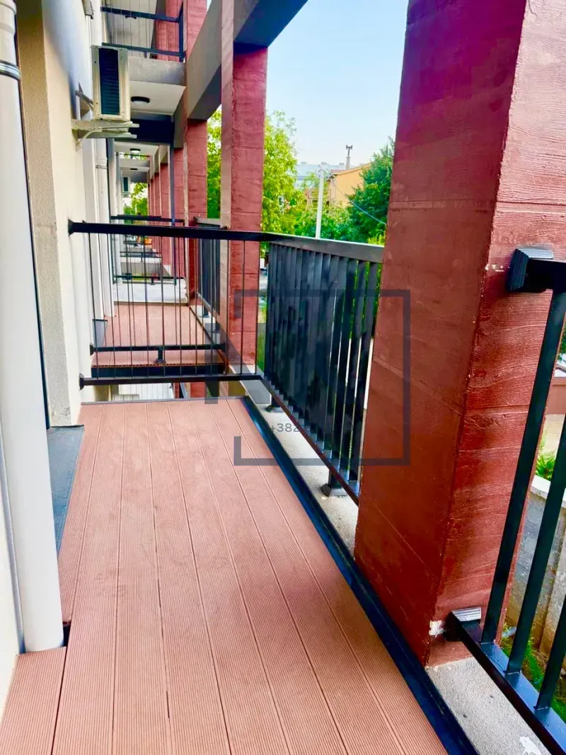 Long wooden balcony with a black railing and a view of the surroundings.