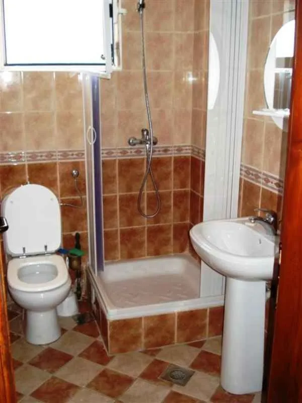 Manje kupatilo sa tuš kabinom, umivaonikom i toalet šoljom obloženo keramičkim pločicama.