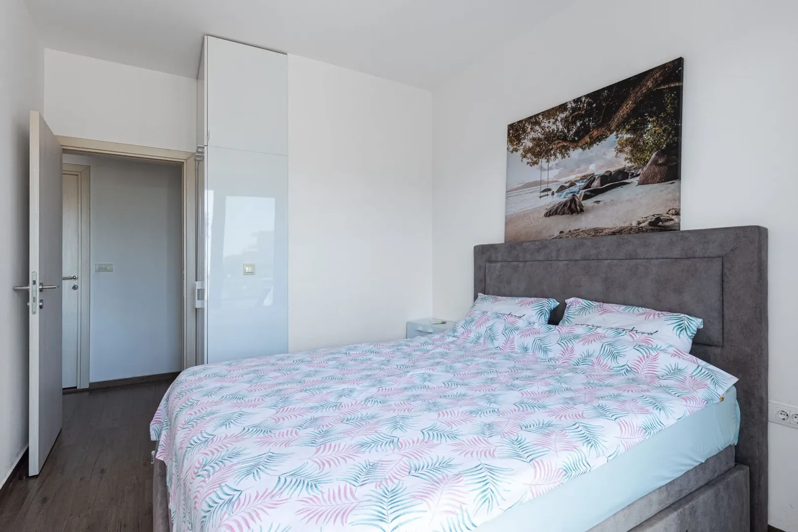 Spavaća soba sa bračnim krevetom, ugradnim plakarom i umjetničkom slikom na zidu.