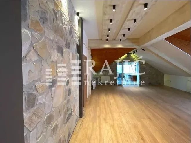 Spacious attic living space with a stone wall and wooden flooring.