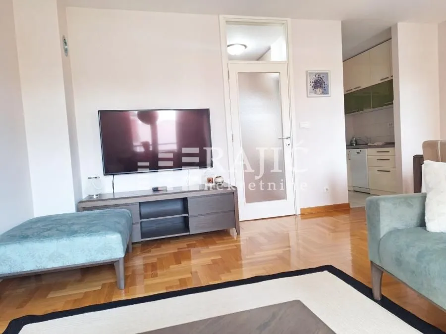 Living room with furniture and TV, overlooking the dining area and kitchen.