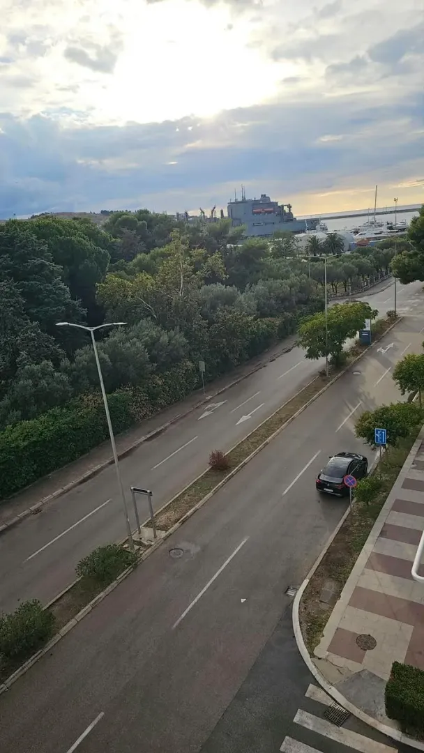Pogled sa terase na ulicu, zelenilo i more u daljini.