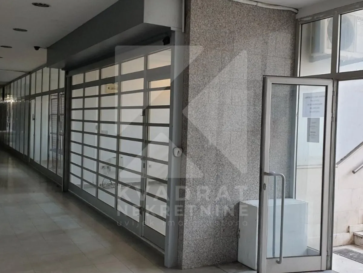 Entrance to the commercial space with glass storefront and roller shutters.