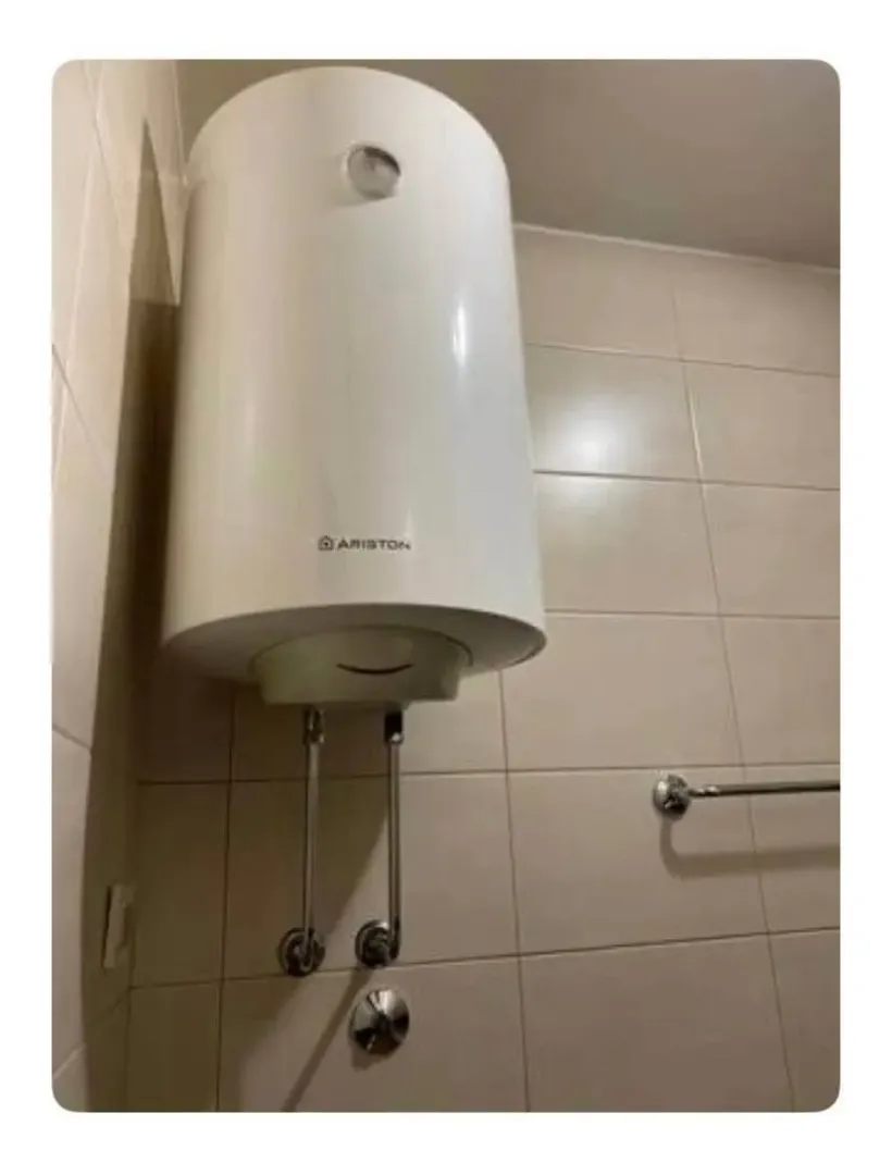 Električni bojler montiran na zid obložen keramičkim pločicama u kupatilu.