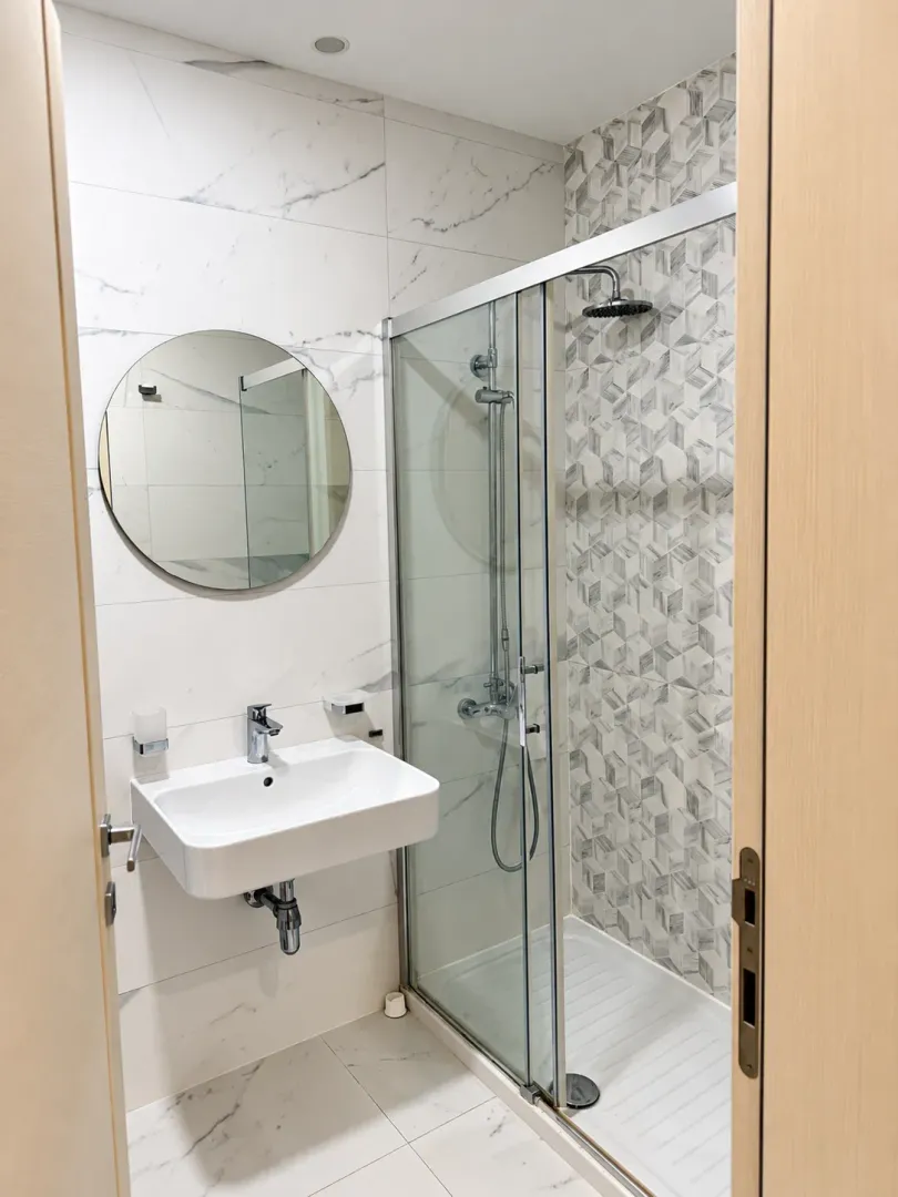 Modern bathroom with a walk-in shower, washbasin, and round mirror.