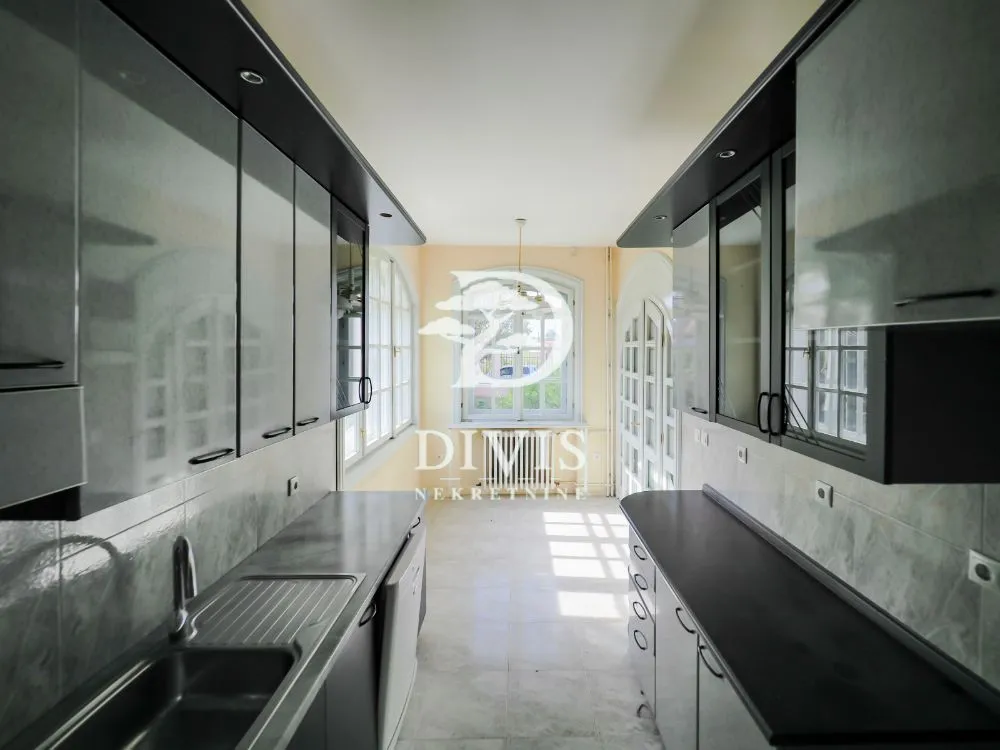 Long kitchen with dark cabinets and a large window at the end of the room.