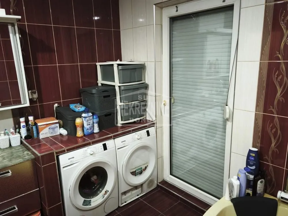 Kupatilo sa veš mašinom i keramičkim pločicama u tamnim tonovima.
