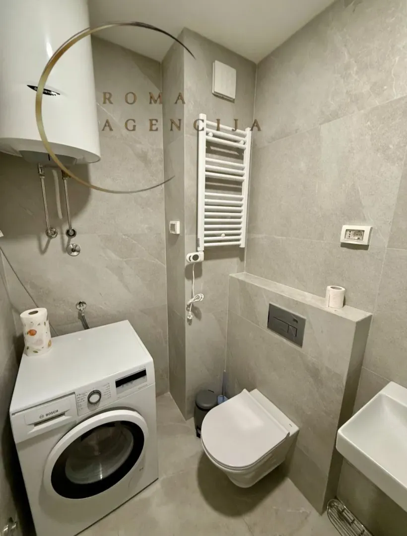 Moderno opremljeno kupatilo sa veš mašinom i tušem.