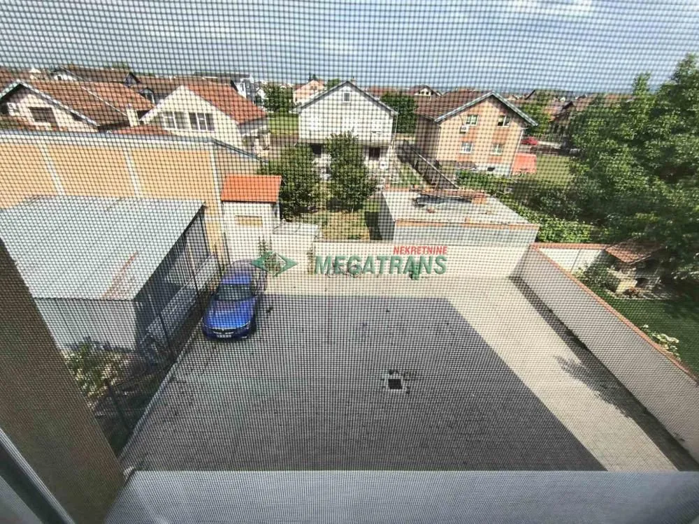 Pogled kroz prozor na dvorište i okolne kuće.