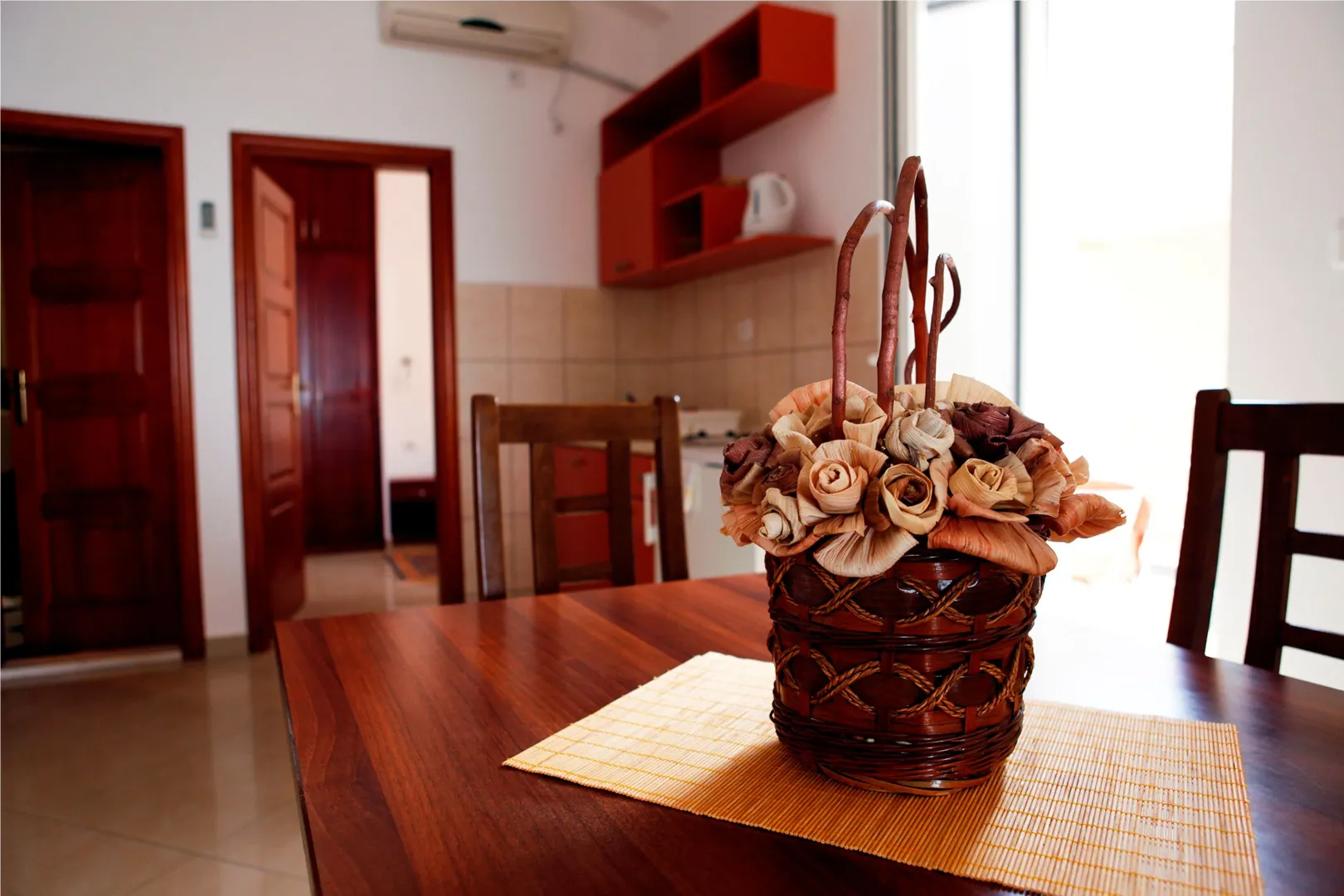 Dining table with a decorative basket and a view of the kitchen in the background.