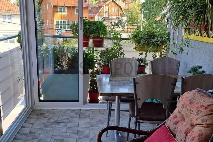 Namešten balkonski prostor sa stolom, stolicama i brojnim saksijama cveća.