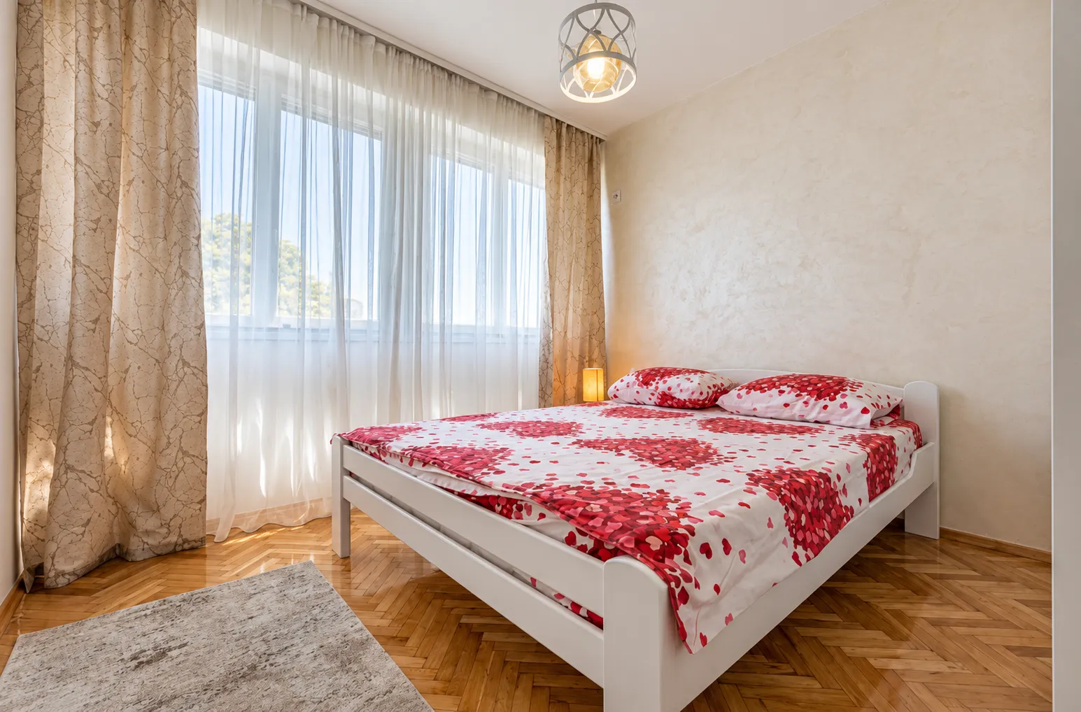 Bedroom with a double bed, parquet flooring, and a window with curtains.
