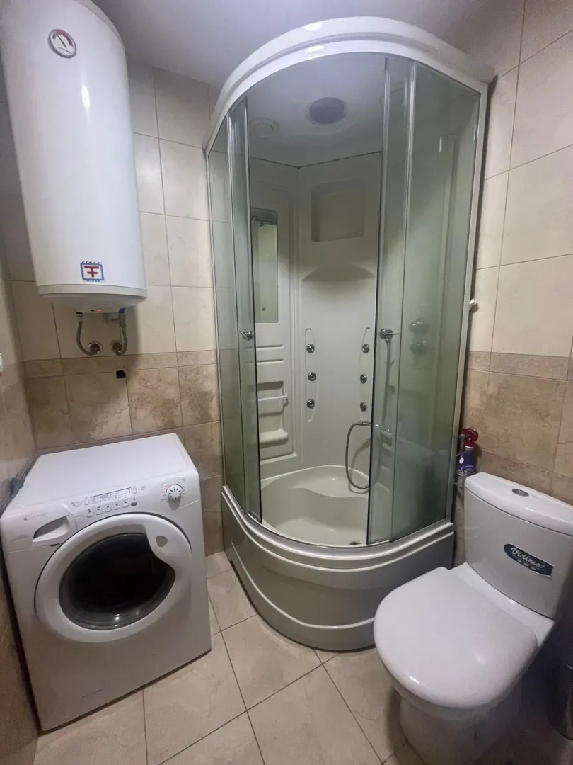 Compact bathroom with a shower cabin, toilet, washing machine, and water heater.