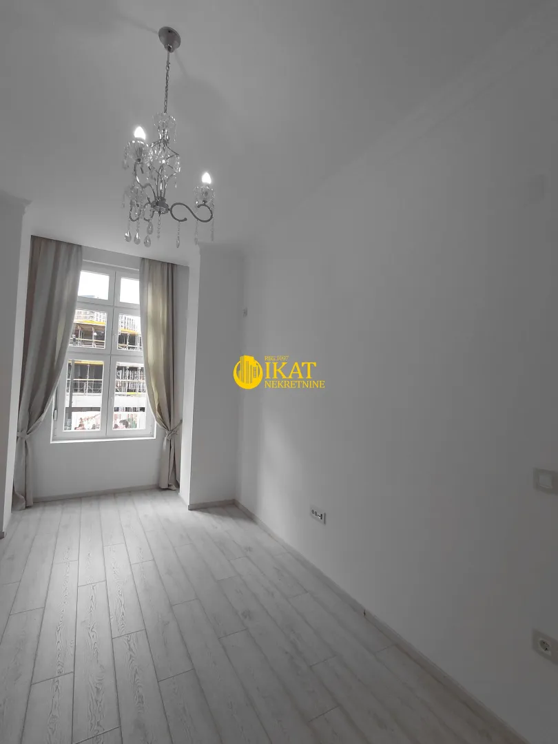 Empty room with white walls, a window, and a chandelier.