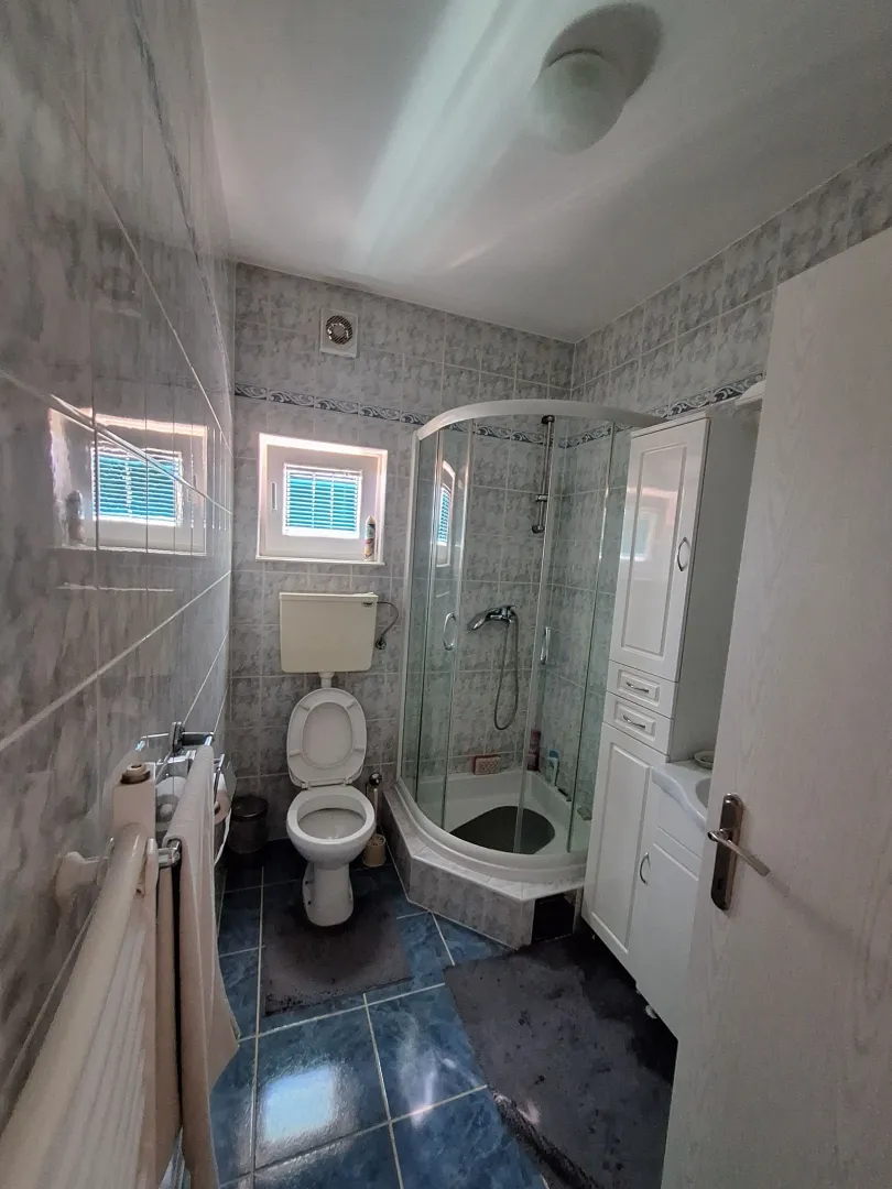 Manje kupatilo sa tuš kabinom, WC šoljom i belim ormarićem.