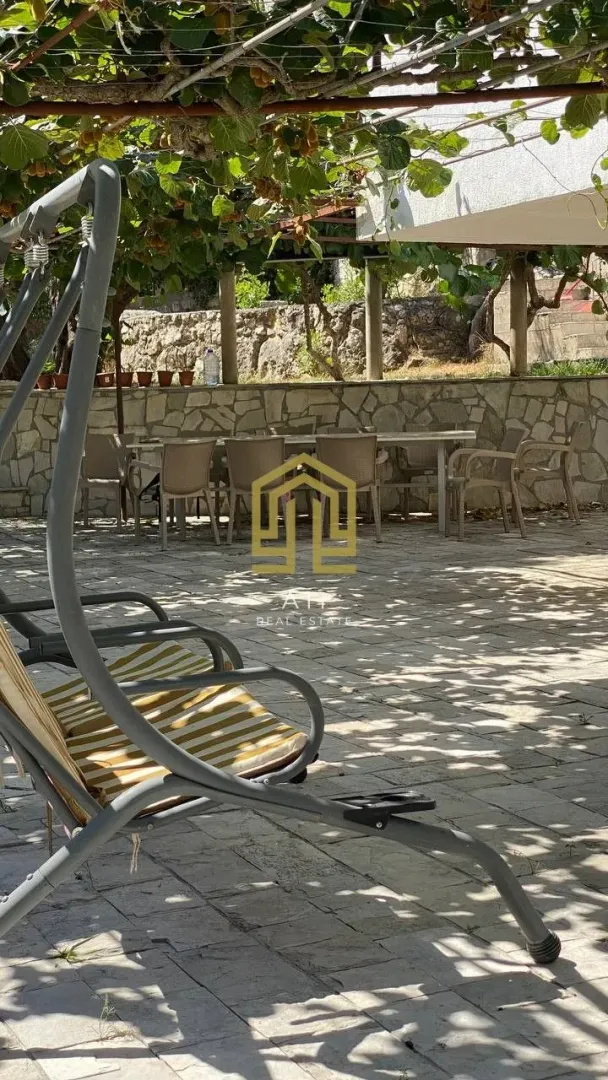 Popločano dvorište sa garniturom za sjedenje i ljuljaškom u hladu vinove loze.