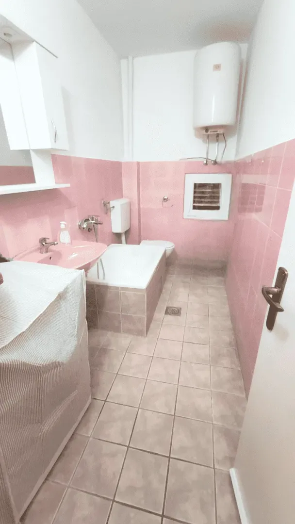 Kupatilo sa roze pločicama, kadom, umivaonikom i bojlerom.