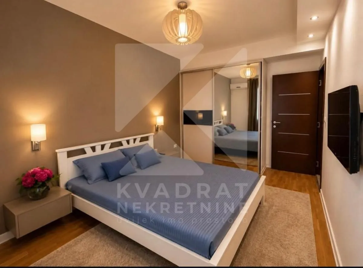 Namještena spavaća soba sa bračnim krevetom, plakarom sa ogledalom i televizorom.