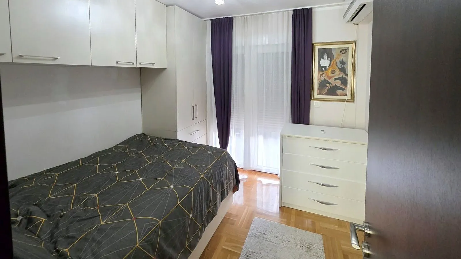 Manja spavaća soba sa krevetom, ugradnim plakarom i komodom.