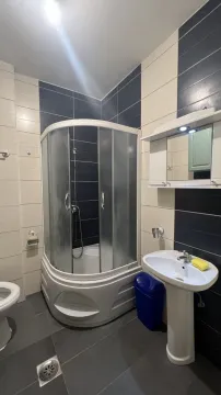 A simple bathroom featuring a corner shower cabin, pedestal sink, and two-tone tiling. - image 12