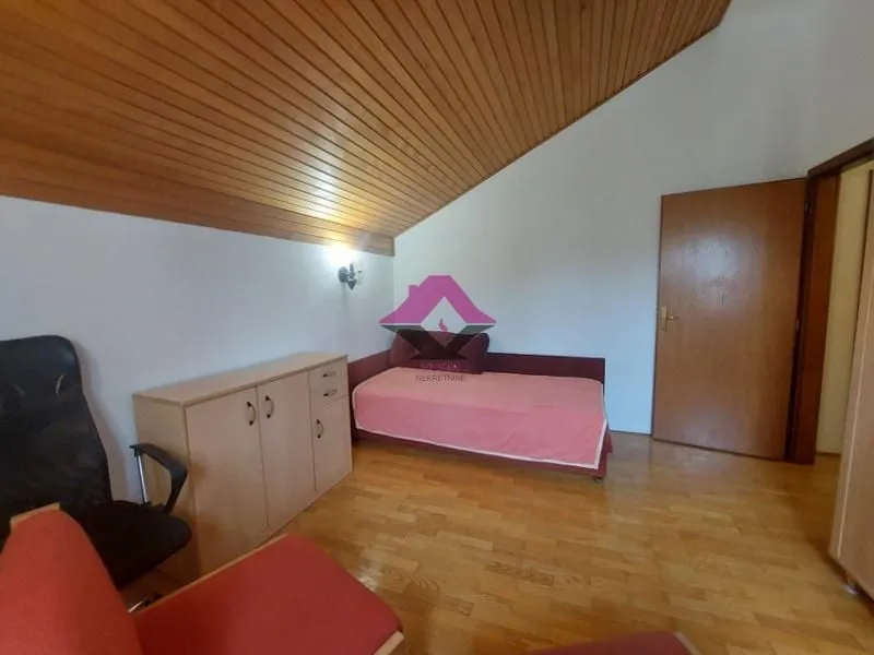 Nameštena spavaća soba sa kosim drvenim plafonom i drvenim podom.