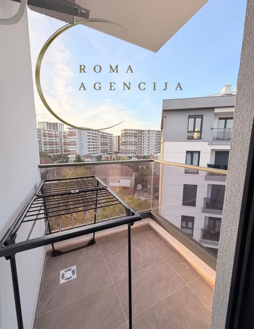 Manji popločani balkon sa stalkom za sušenje veša i pogledom na zgrade.