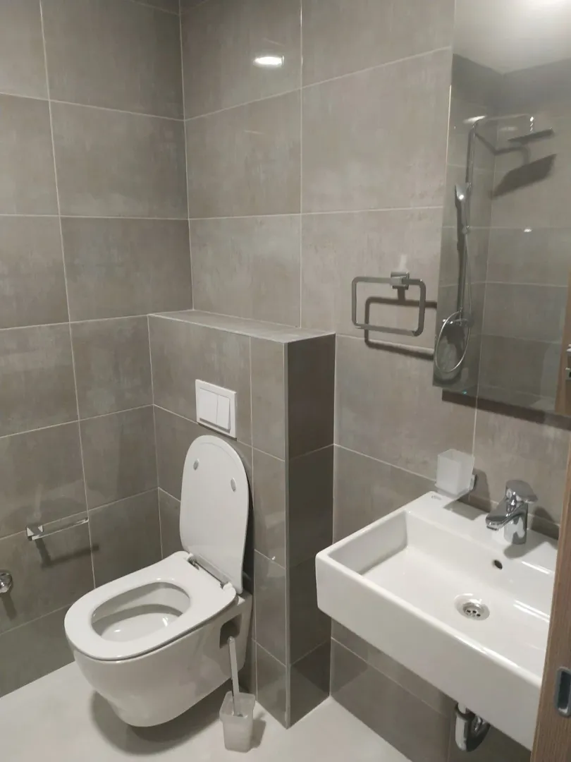 Moderno kupatilo sa toaletom, umivaonikom i sivim pločicama.