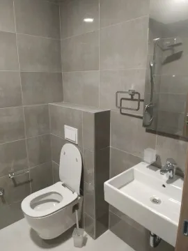 Moderno kupatilo sa toaletom, umivaonikom i sivim pločicama. - image 8
