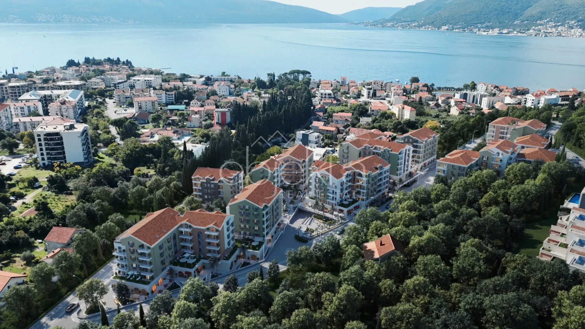 Pogled iz vazduha na kompleks zgrada okružen zelenilom u blizini mora.