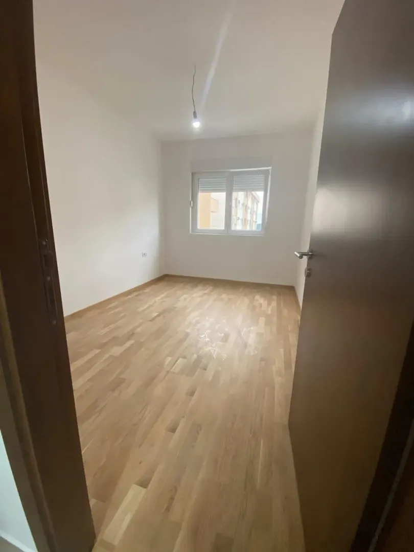Prazna soba sa parketom i prozorom, gledana sa vrata.