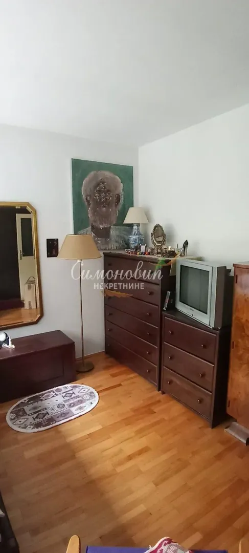 Dnevna soba sa drvenim komodama, televizorom i umetničkom slikom na zidu.