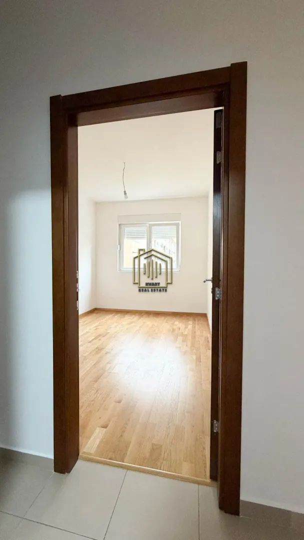 Pogled kroz vrata na praznu sobu sa drvenim podom.