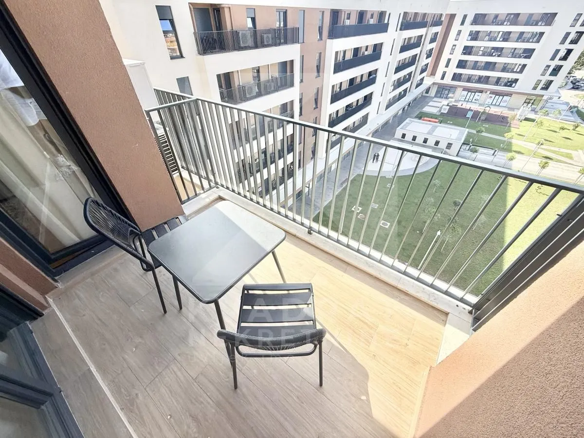 Manji namješteni balkon sa stolom i dvije stolice i pogledom na dvorište zgrade.