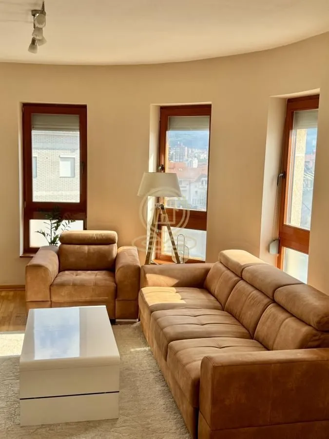Living room with a sofa, armchair, coffee table, and windows with city views.
